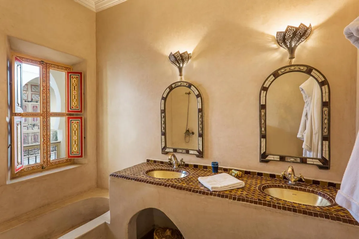A tadelakt bathroom with an artisan mirror and brass sconce