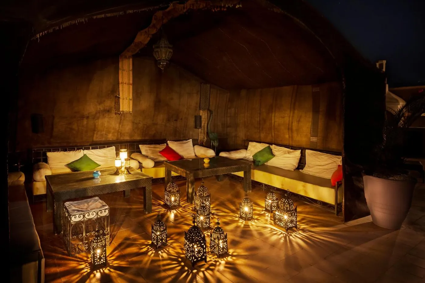 The dining salon at night: lantern shadows across the walls, tables set below the arches