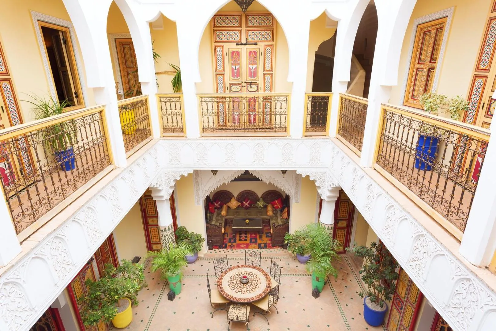 The double gallery of the courtyard in daylight: white arcades, painted doors, wrought-iron rails