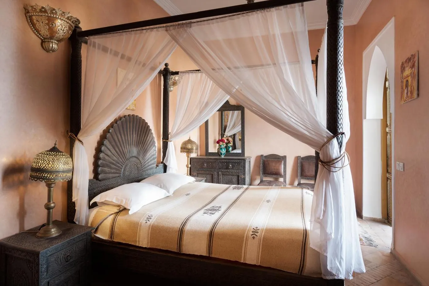 A carved four-poster bed under white voile, blush tadelakt walls