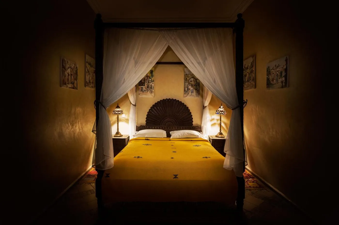 A dark carved four-poster with saffron bedding